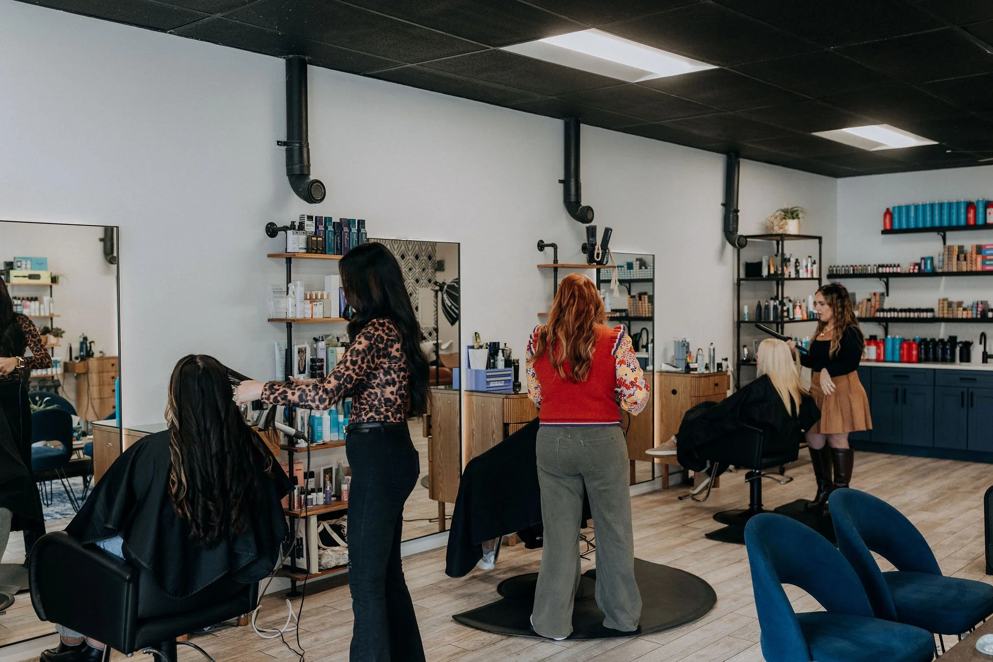 Interior of a hair salon with two hairstylists working on clients and shelves stocked with hair products.