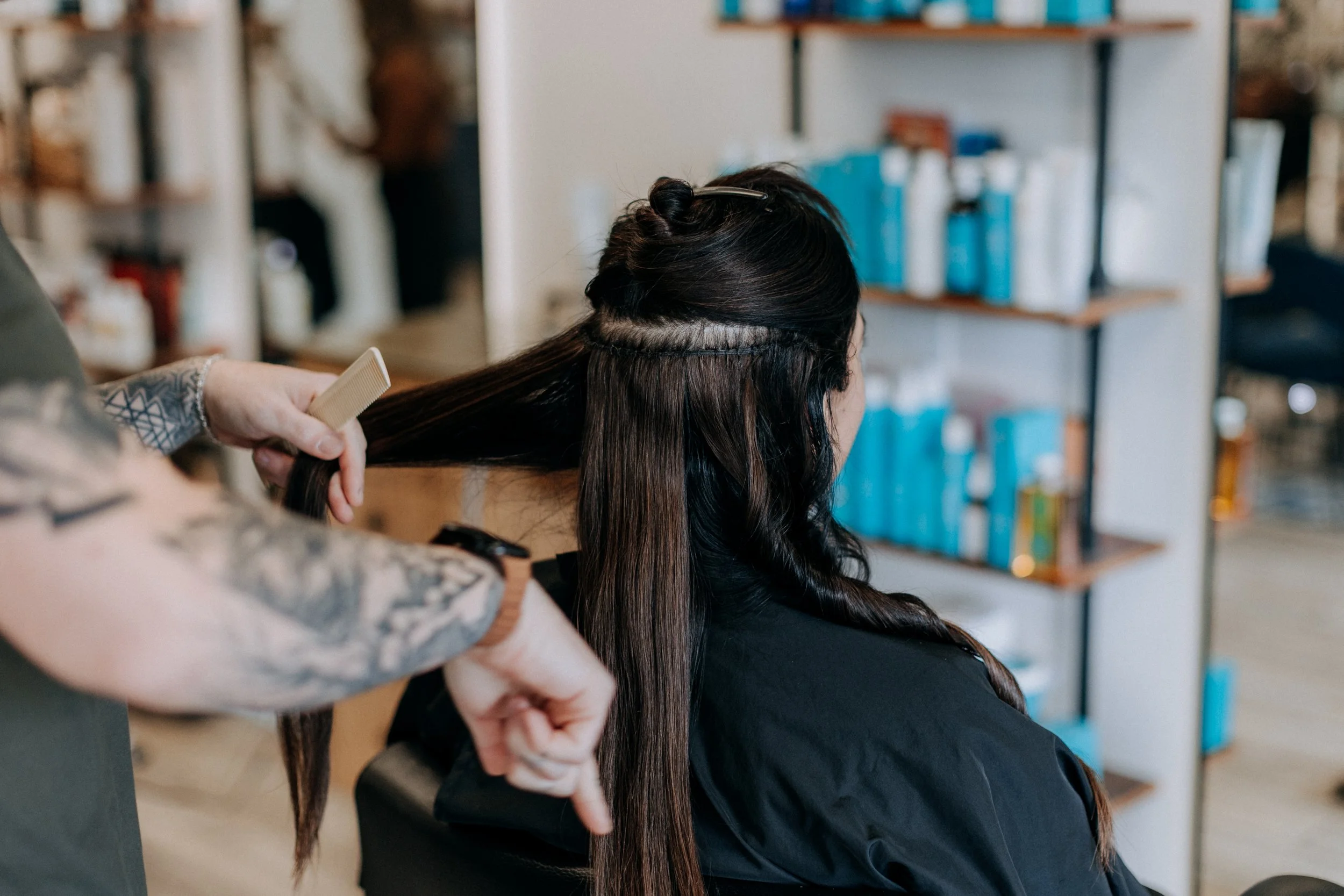 Hairdresser styling a woman's long dark hair in a salon.
