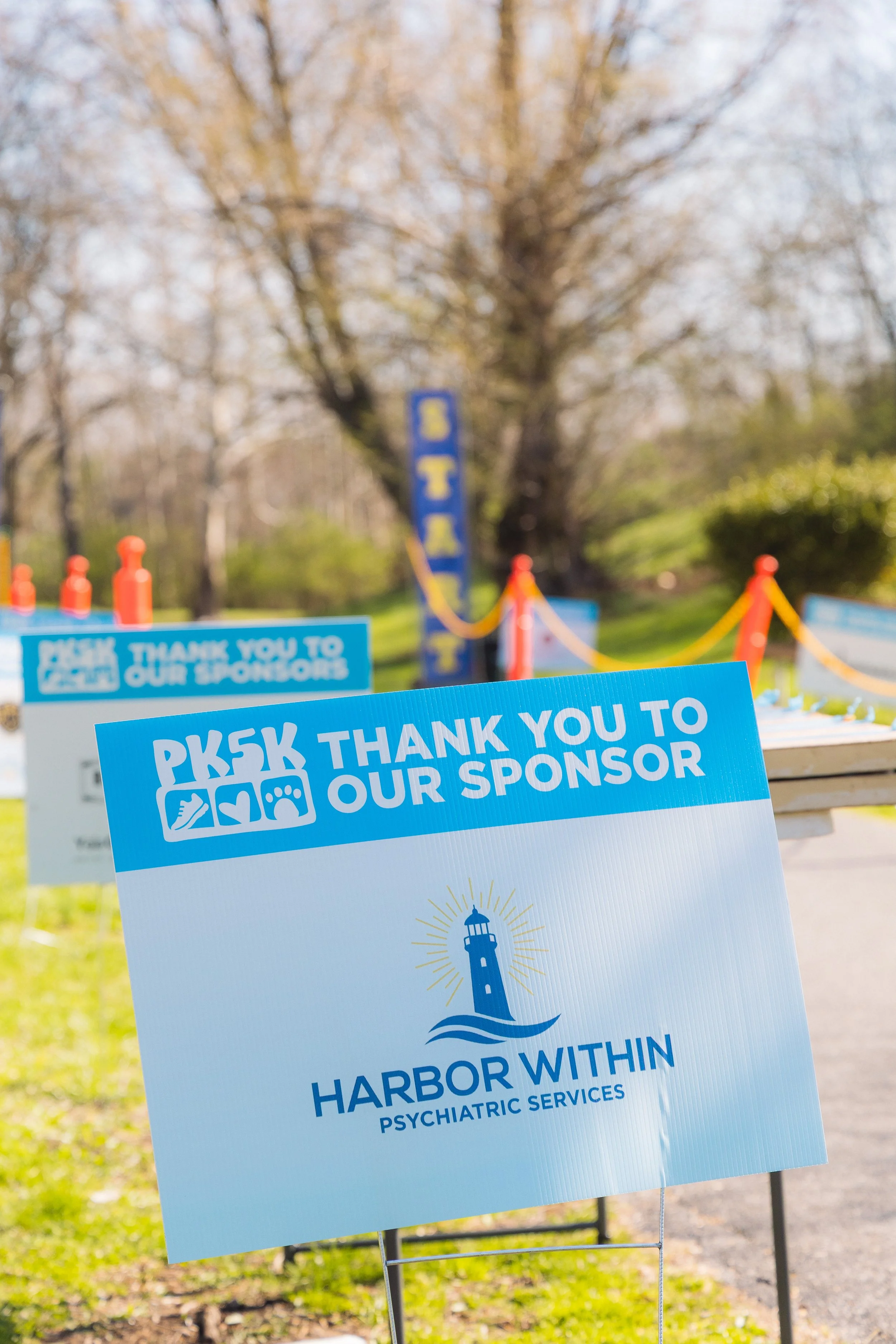 Signs with messages of gratitude for sponsors and support for the harbor within psychiatric services, set up outdoors near trees and greenery.