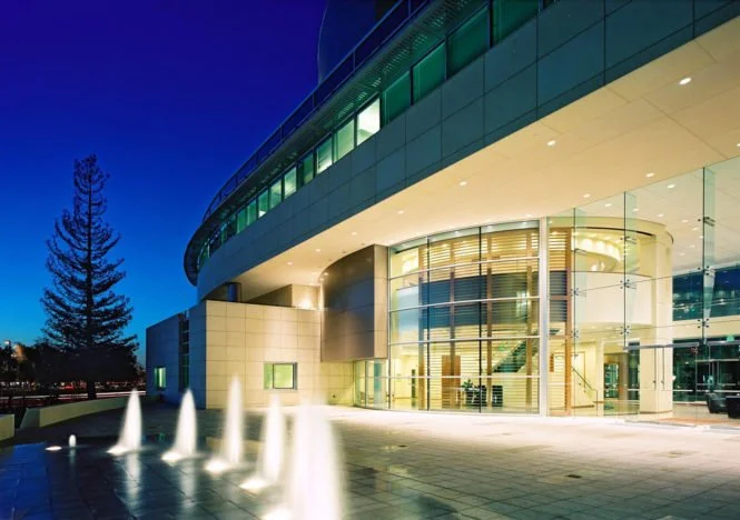 Modern building with curved glass facade and water fountain at night.