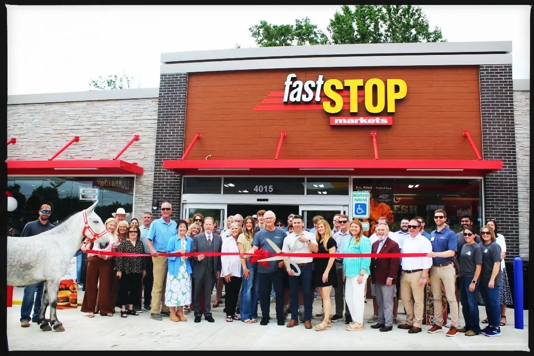 Group of people attending the grand opening of a Fast Stop Markets store, with some holding scissors for a ribbon-cutting ceremony, in front of the store's entrance.