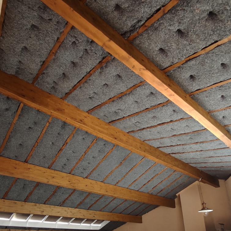 Plafond en construction avec poutres en bois et isolant en laine de roche ou mousse.
