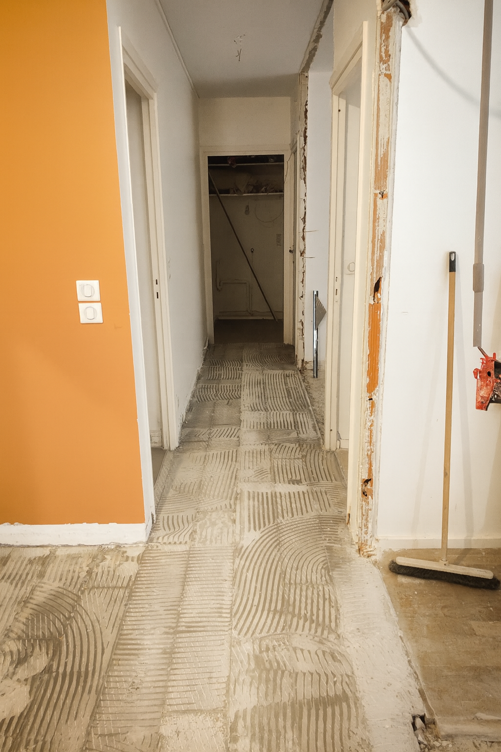 Passage d'une rénovation intérieure avec sol en cours de pose, murs partiellement démolis et outils de construction à côté.