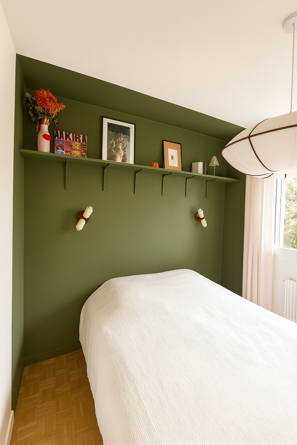 Chambre avec mur vert, lit avec couverture blanche, étagère avec décorations, tableaux et lampes murales.