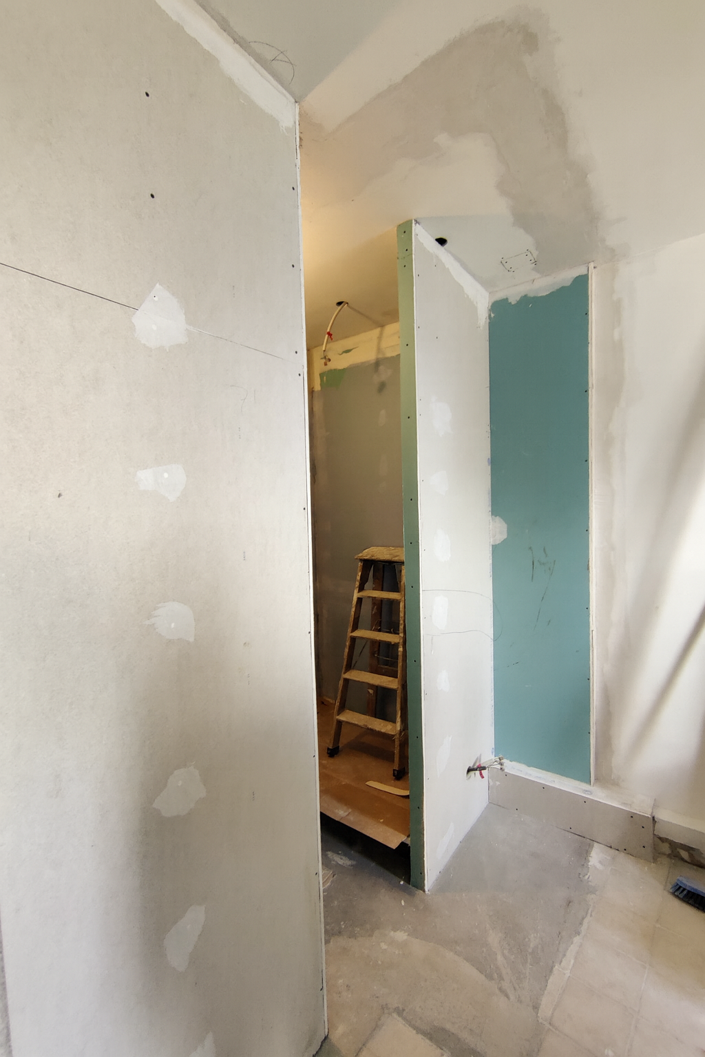 Intérieur en cours de rénovation avec des murs en plâtre partiellement installés et un escabeau en bois.