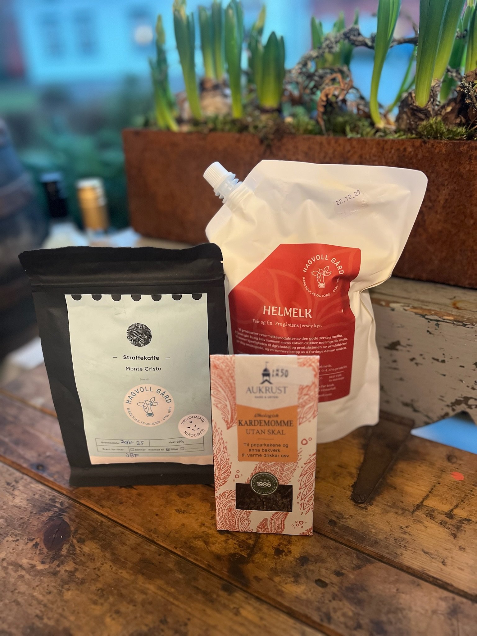 Kaffe, te og krydderi på et trebord med en planteløk i bakgrunnen.