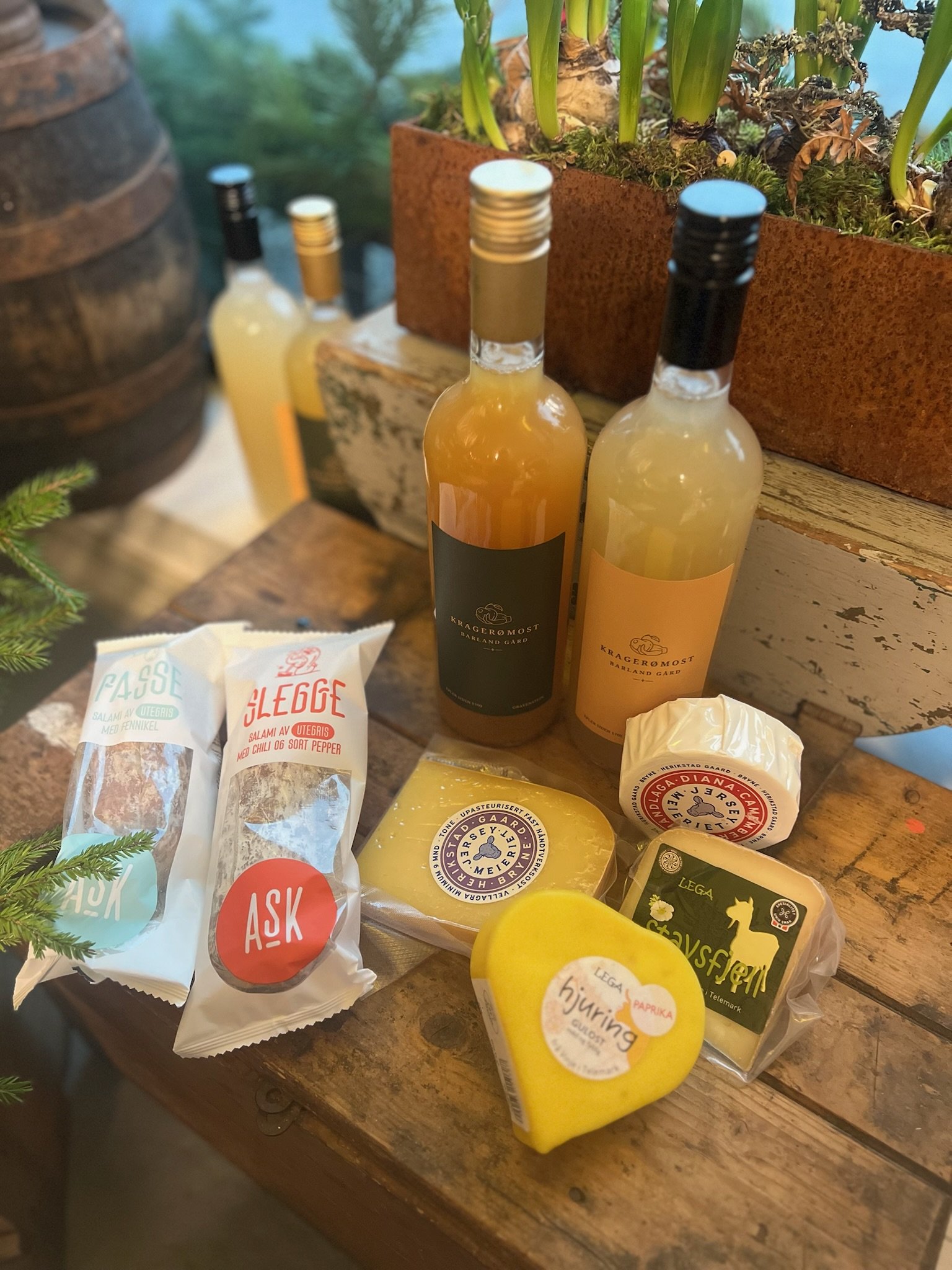 Ulike oster, pølser og drikkevarer på et rustikt trebord.