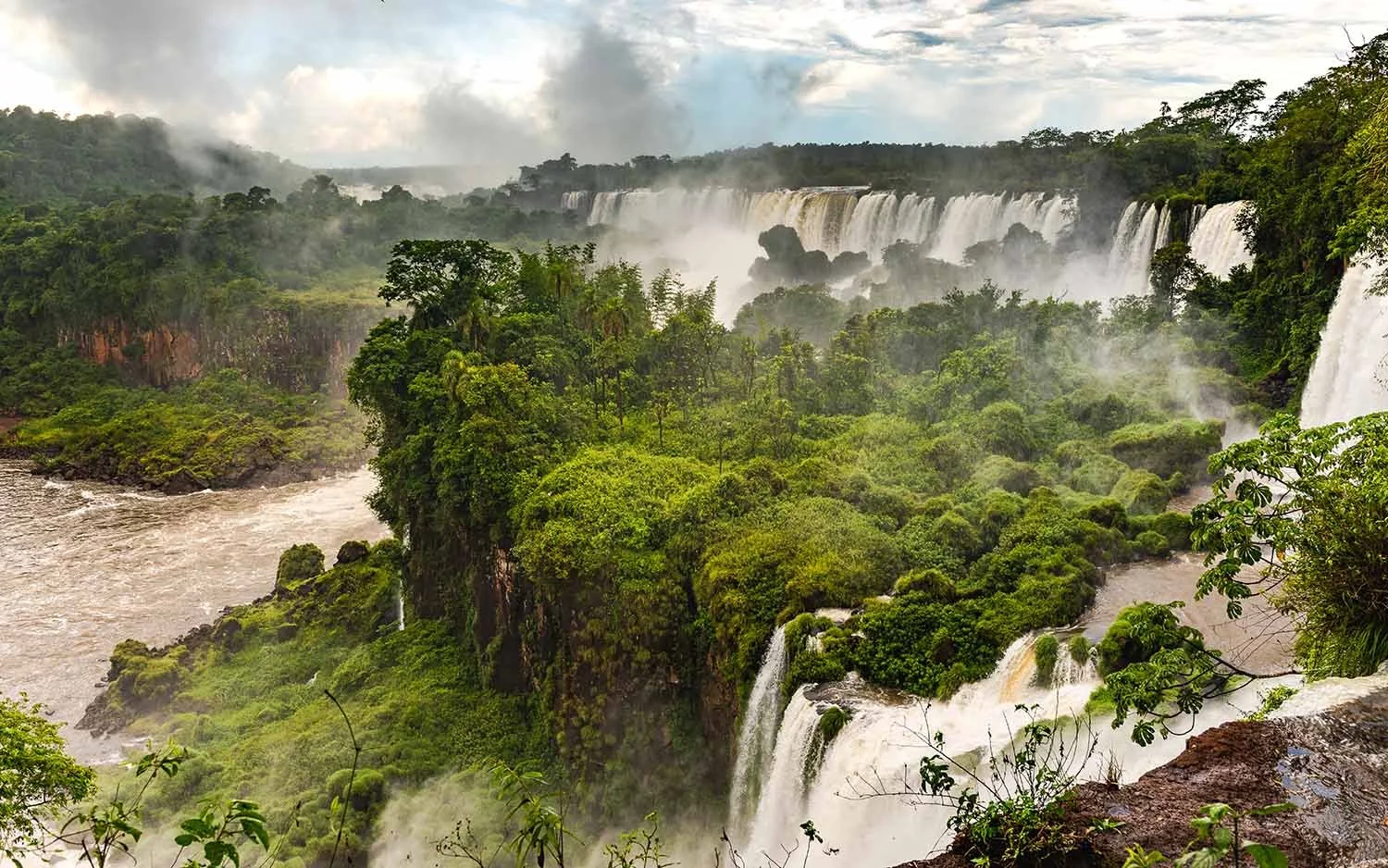 View of Iguazu Falls surrounded by lush green forest with cascading waterfalls and mist in the air.