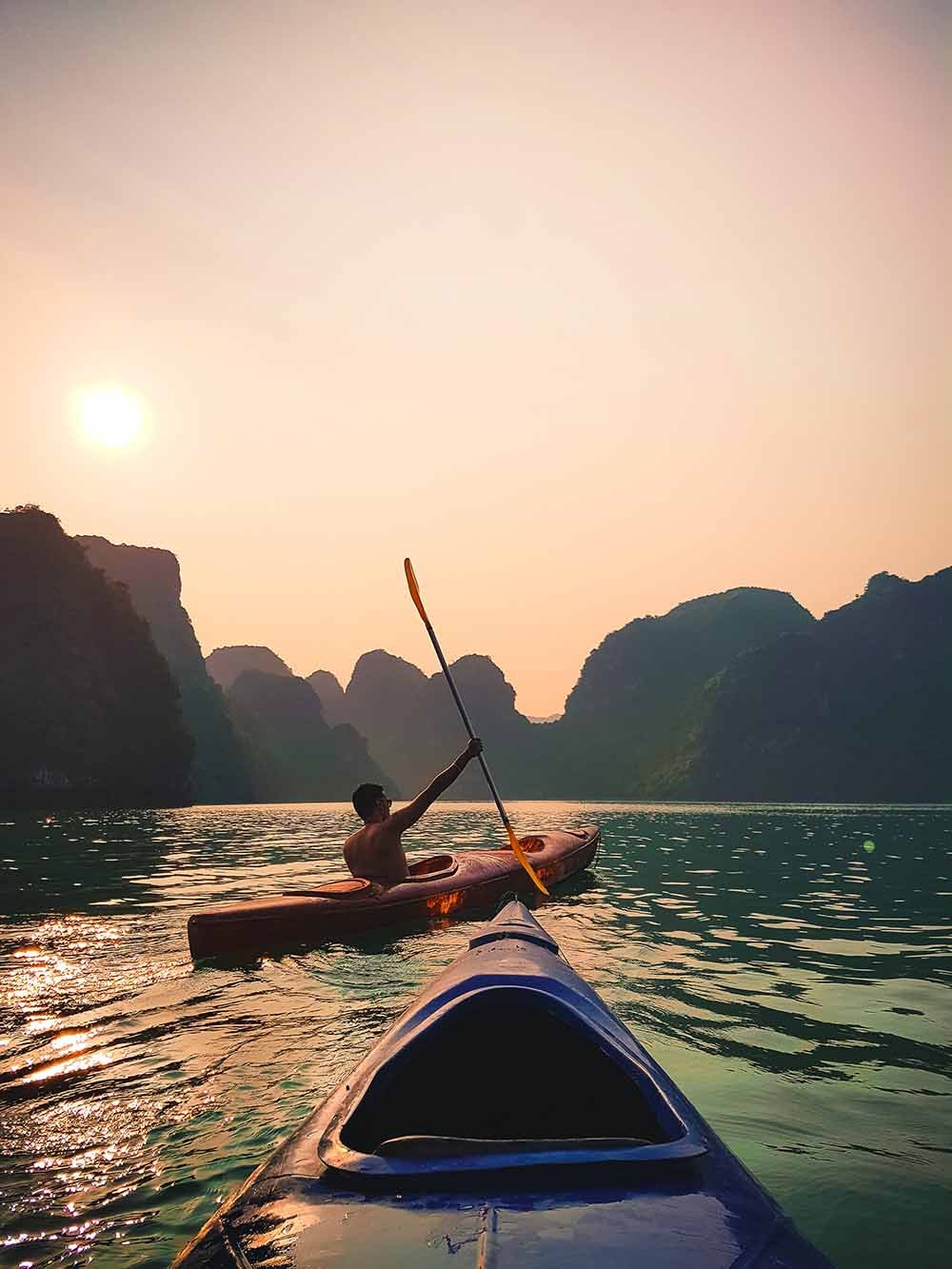 A person kayaking on calm waters during sunset with limestone cliffs in the background.