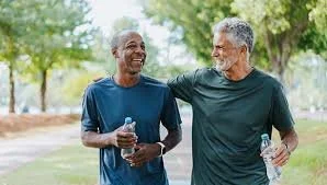 Two older men walking in a park, smiling and talking, one holding a water bottle