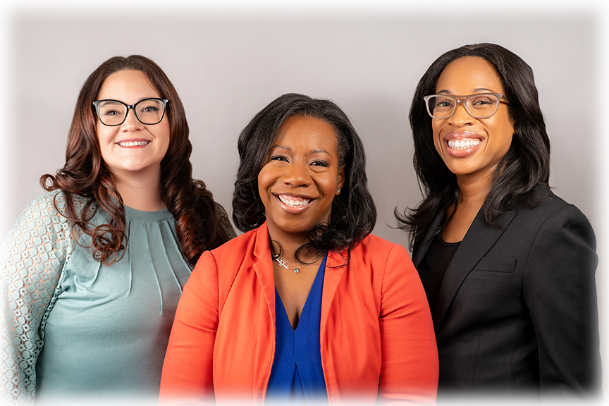 Three women smiling, dressed in professional attire, standing against a gray background.