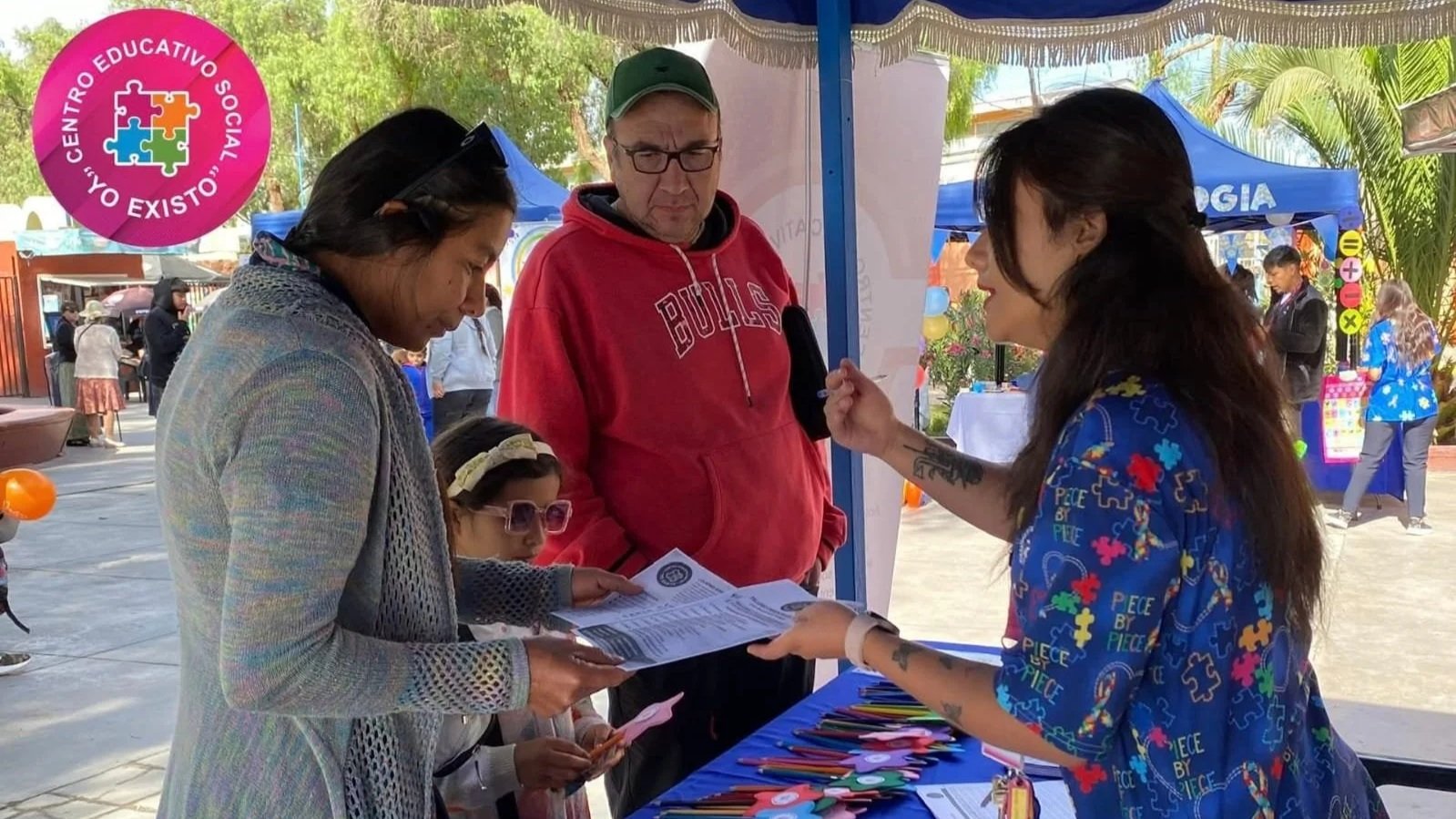 Personas en un puesto informando y distribuyendo folletos en un evento al aire libre.