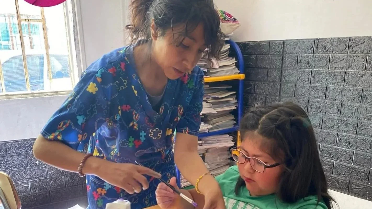 Una mujer llamada enfermera o doctora administrando una inyección a una niña con gafas en un consultorio.
