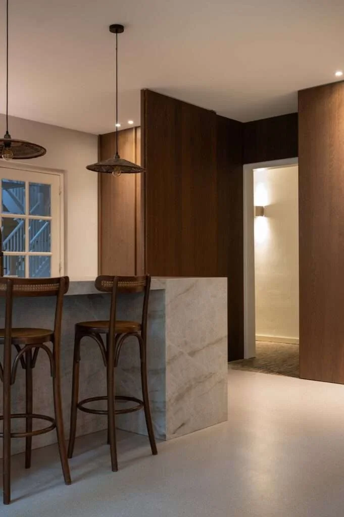Intérieur moderne avec un comptoir en marbre, deux chaises en bois, des lampes suspendues en osier et un mur en bois.