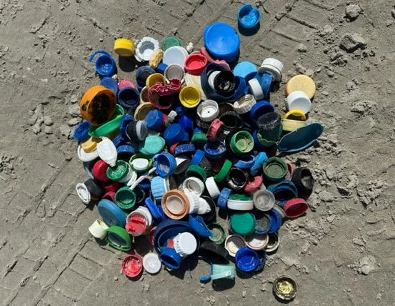 A pile of various plastic bottle caps on dirt ground.