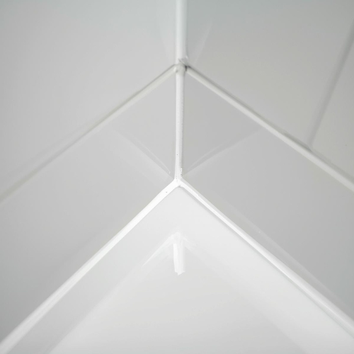 A close up of a corner of tile above a bathtub with crisp, white caulking.