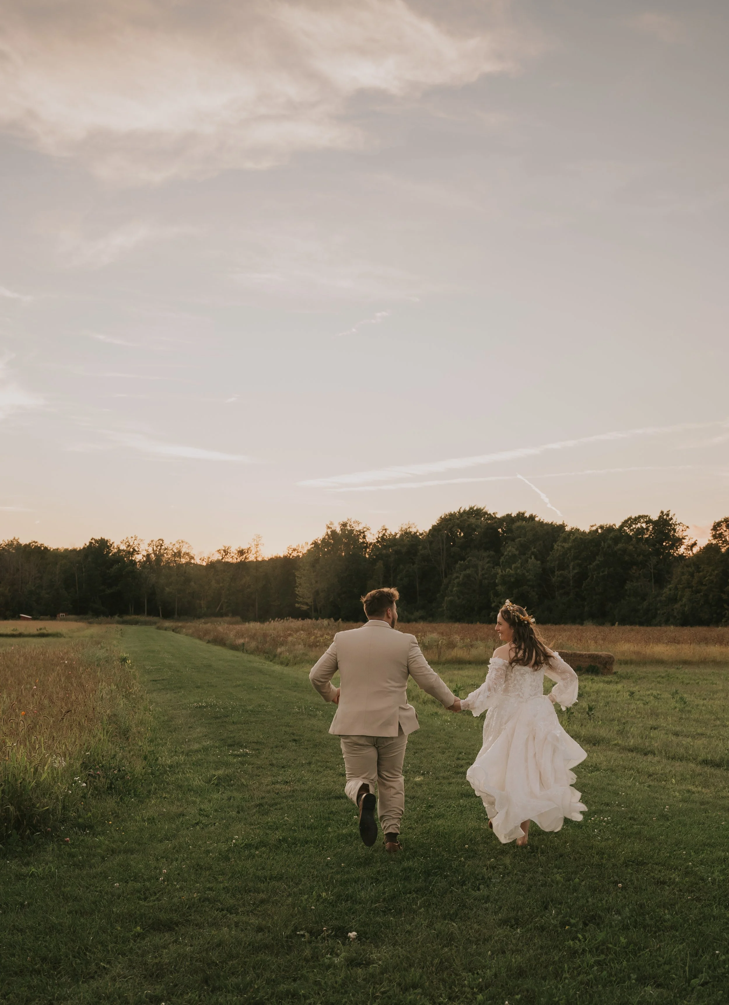 A newlywed couple celebrating outside at night in a snowy setting, with champagne, as snow falls around them, in front of a building with a sign.