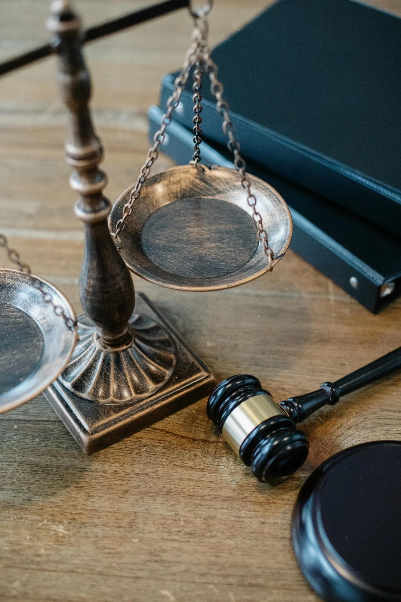 A set of metallic legal symbols on a wooden surface, including a gavel, scales of justice, and a legal case file.
