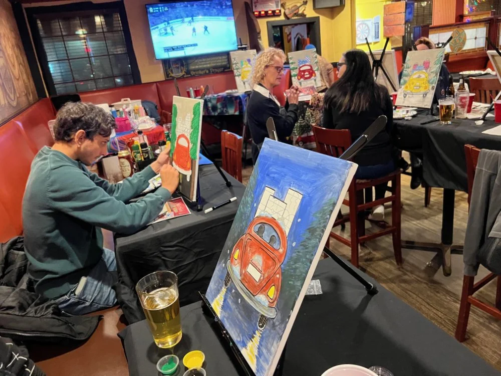 People painting colorful artworks of cars on canvases at a painting event in a restaurant.