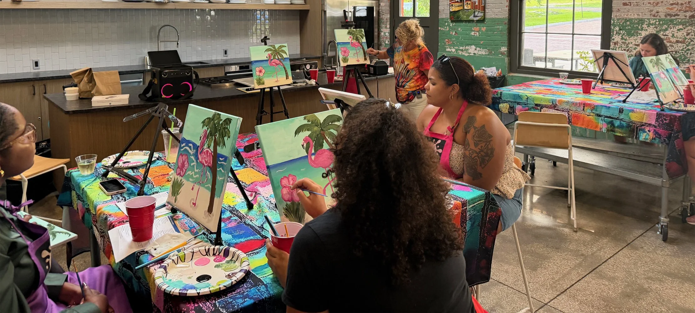 People participating in a painting class, creating artwork featuring pink flamingos, palm trees, and tropical scenery.