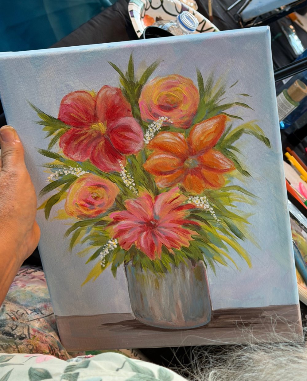 A watercolor painting of a vibrant flower bouquet in a gray vase, featuring pink, orange, and red flowers with green leaves and small white accents, on a light background.