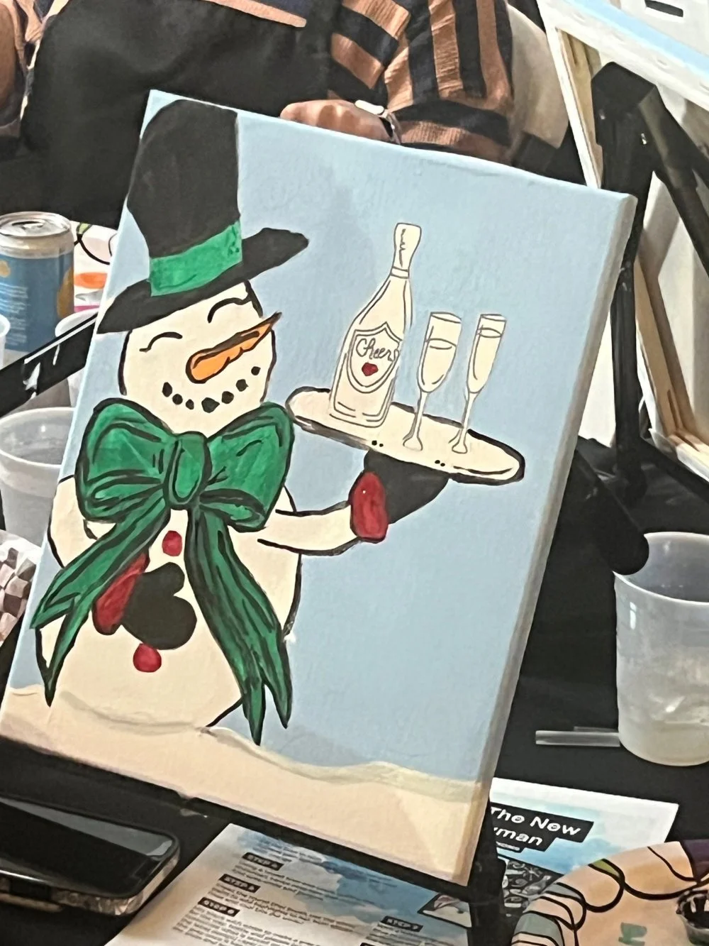 A painting of a snowman wearing a black top hat with a green band, a large green bow tie, and buttons. The snowman is holding a tray with a bottle labeled 'Cheers' and two champagne glasses.