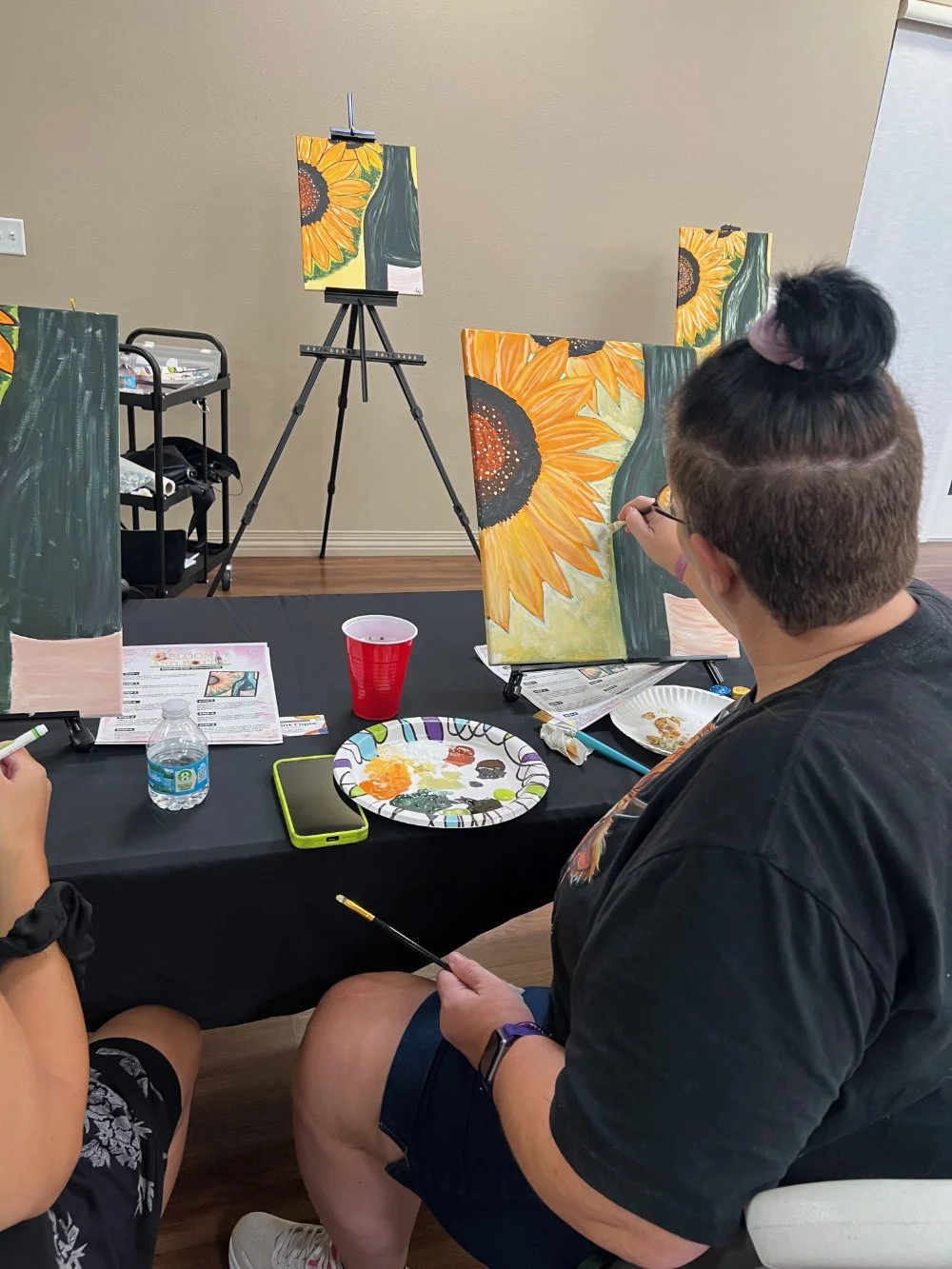 People painting sunflower artwork on canvases during a painting class.