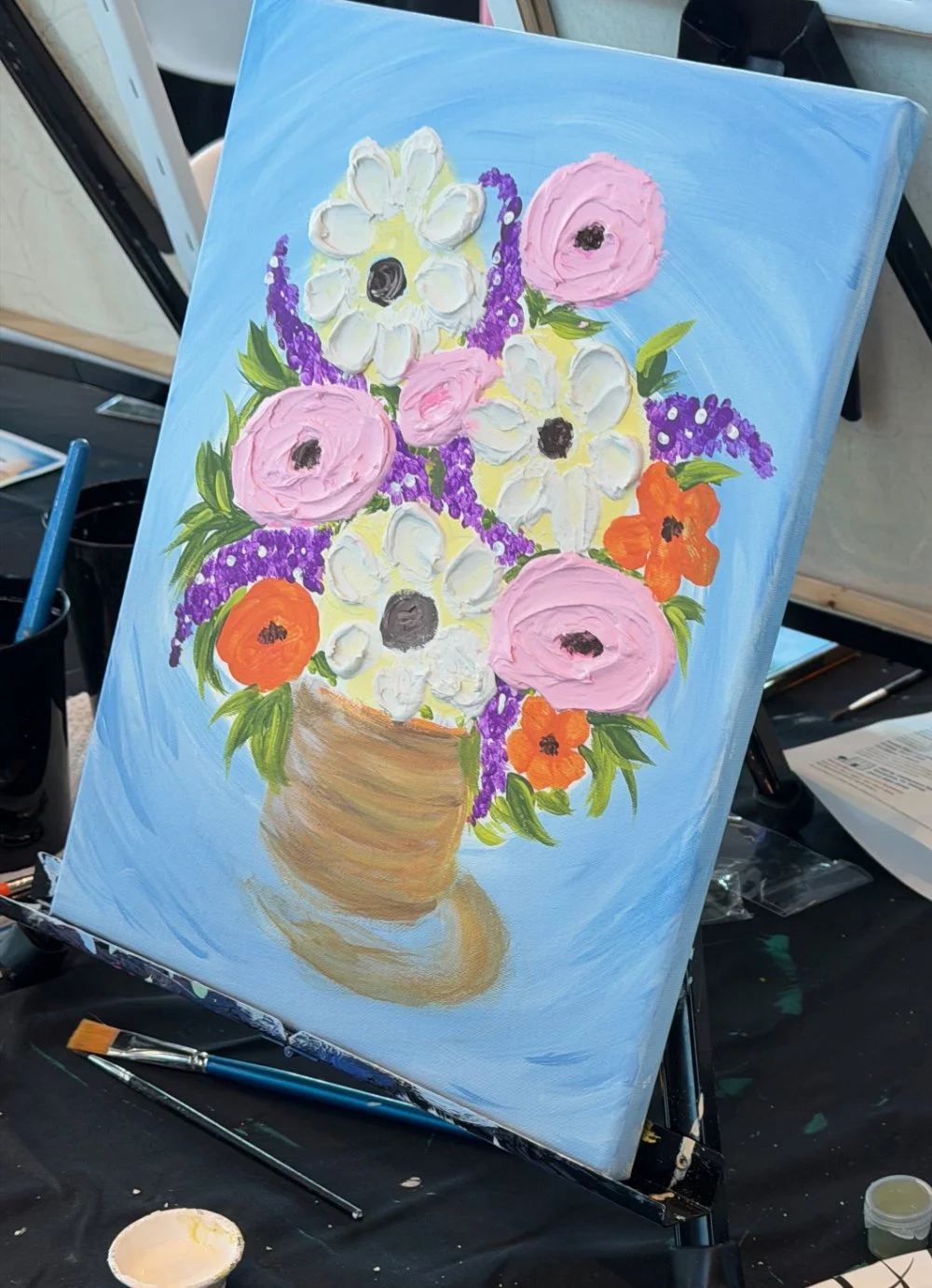 A colorful painting of a flower bouquet in a brown pot, featuring pink, white, orange, and purple flowers with green leaves on a blue background.