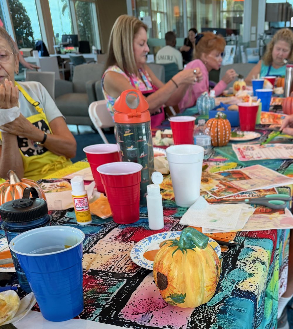 A table with autumn-themed decorations including painted pumpkins and fall-colored tablecloths at a gathering of people dining indoors.