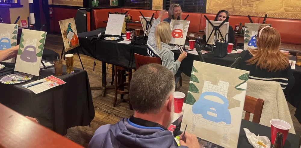 People participating in a painting event at a restaurant, creating paintings of colorful kettlebells on canvas.