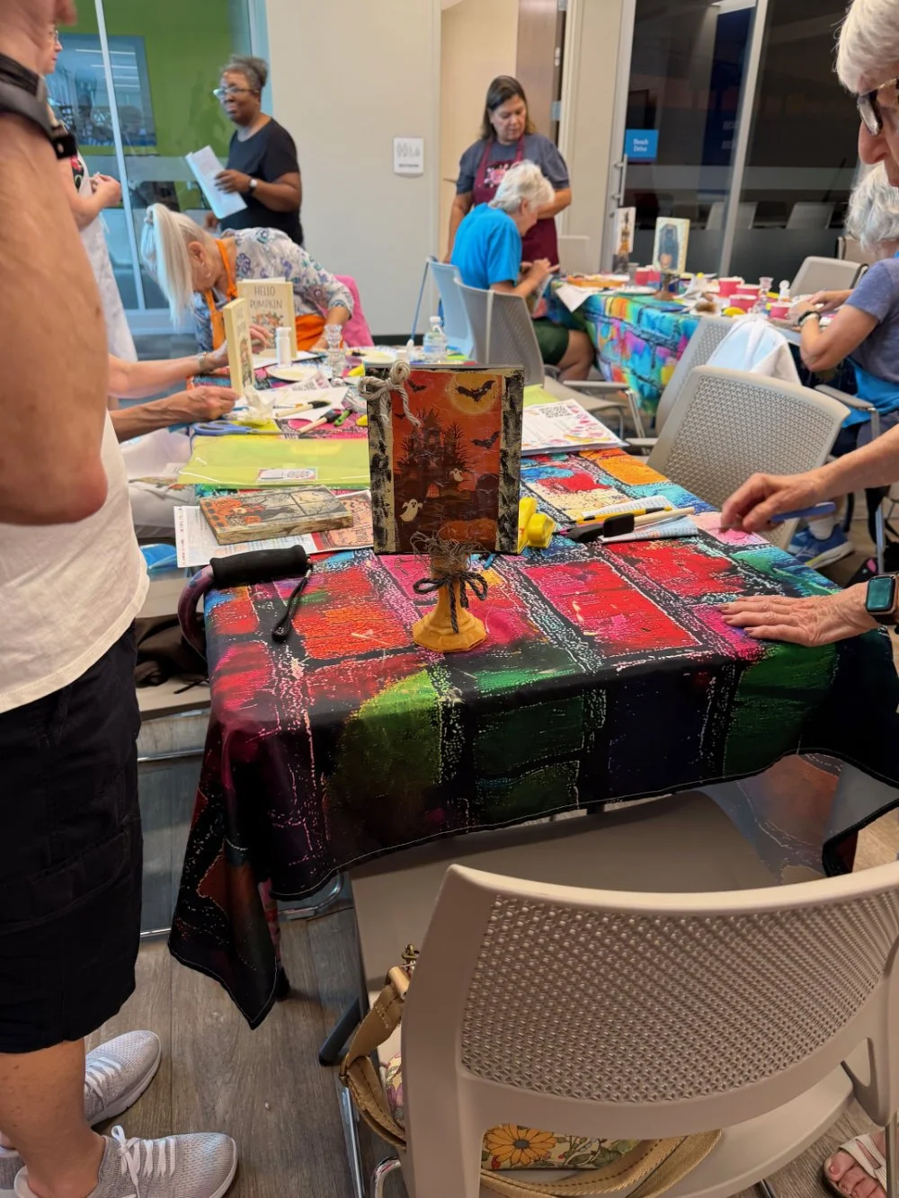 Table decorated with colorful tablecloths at a crafting event, with various craft supplies, art projects, and seasonal decorations displayed.