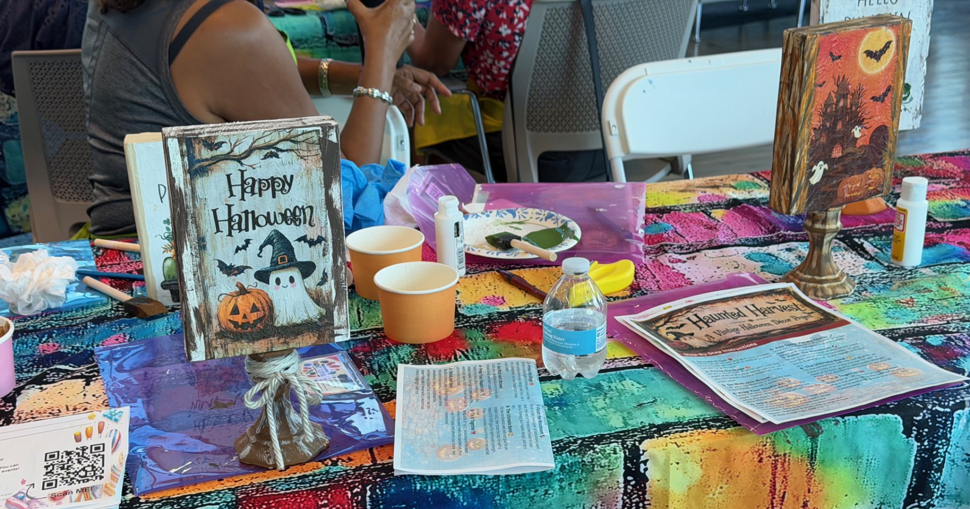 Decorated table with Halloween-themed signs, craft supplies, and instructional sheets at a Halloween craft event.