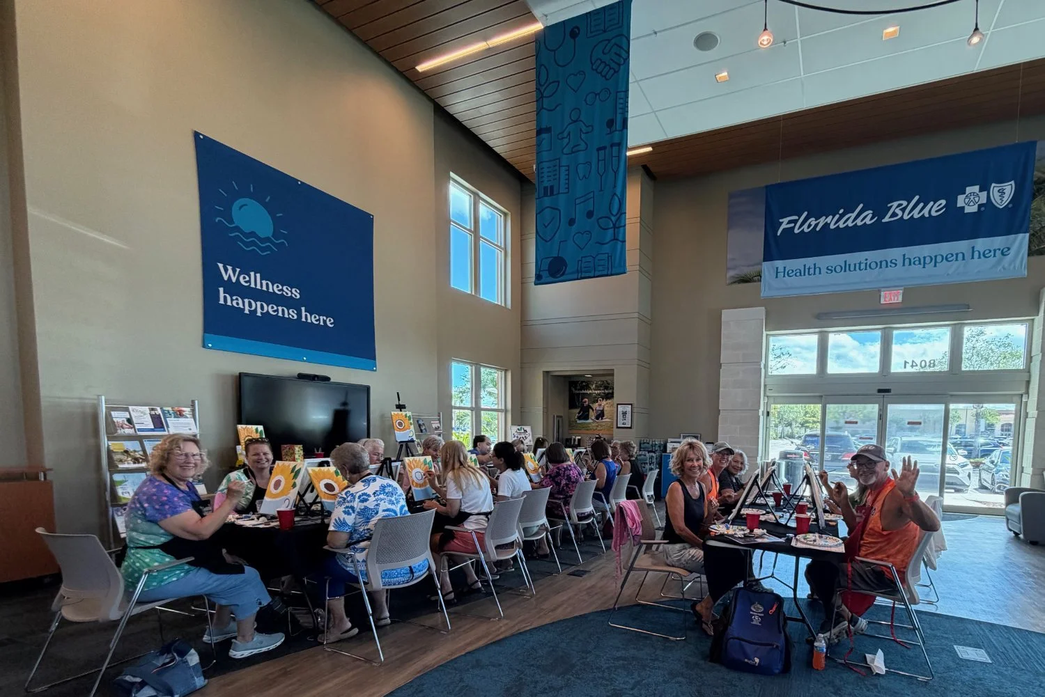 Group of people sitting at tables inside a large, well-lit room with banners that read "Wellness happens here" and "Florida Blue".