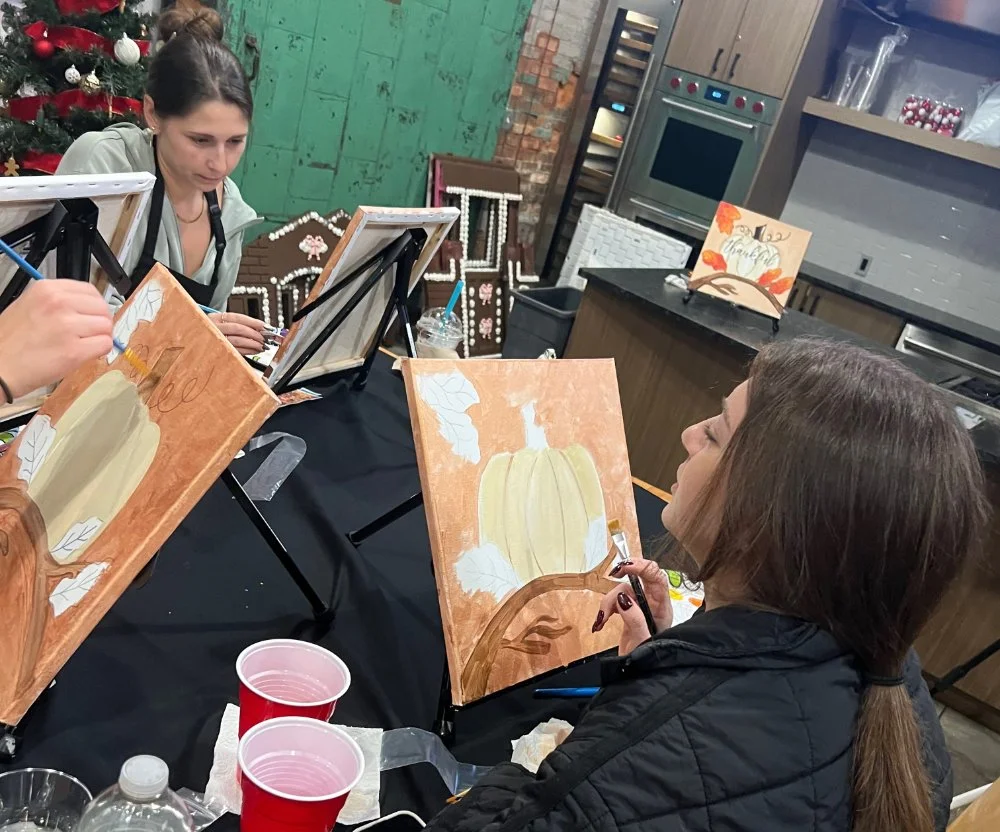 People painting fall-themed pictures with pumpkins in a rustic studio.
