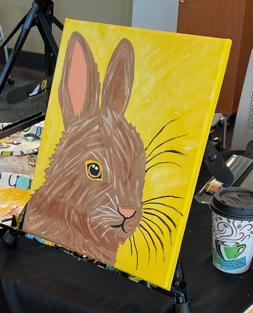 A painting of a rabbit's face on a yellow background, showing brown fur, long ears, and whiskers.