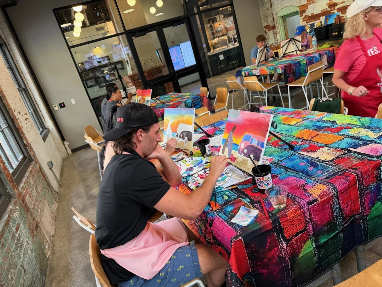 People participating in a painting class at an art studio with colorful tables and paintings.