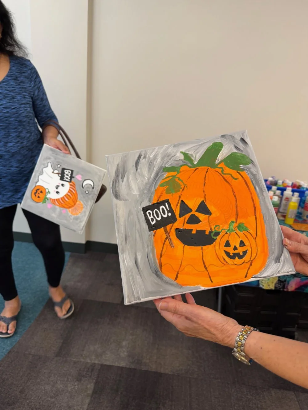 Hand-painted Halloween-themed canvas with a large orange pumpkin and smaller pumpkin with faces, green leaves, and two signs reading 'BOO!' and 'BOO!'.