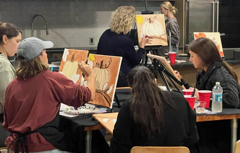 Group of women painting pumpkins on canvases in an art class.