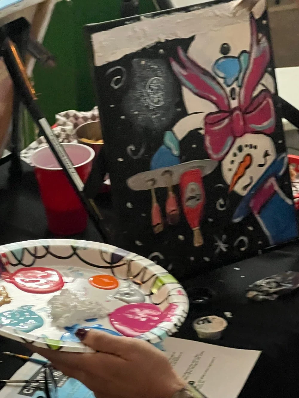 Painting of a clown with a red bow, blue hat, and colorful clock on a canvas, with painting supplies around.