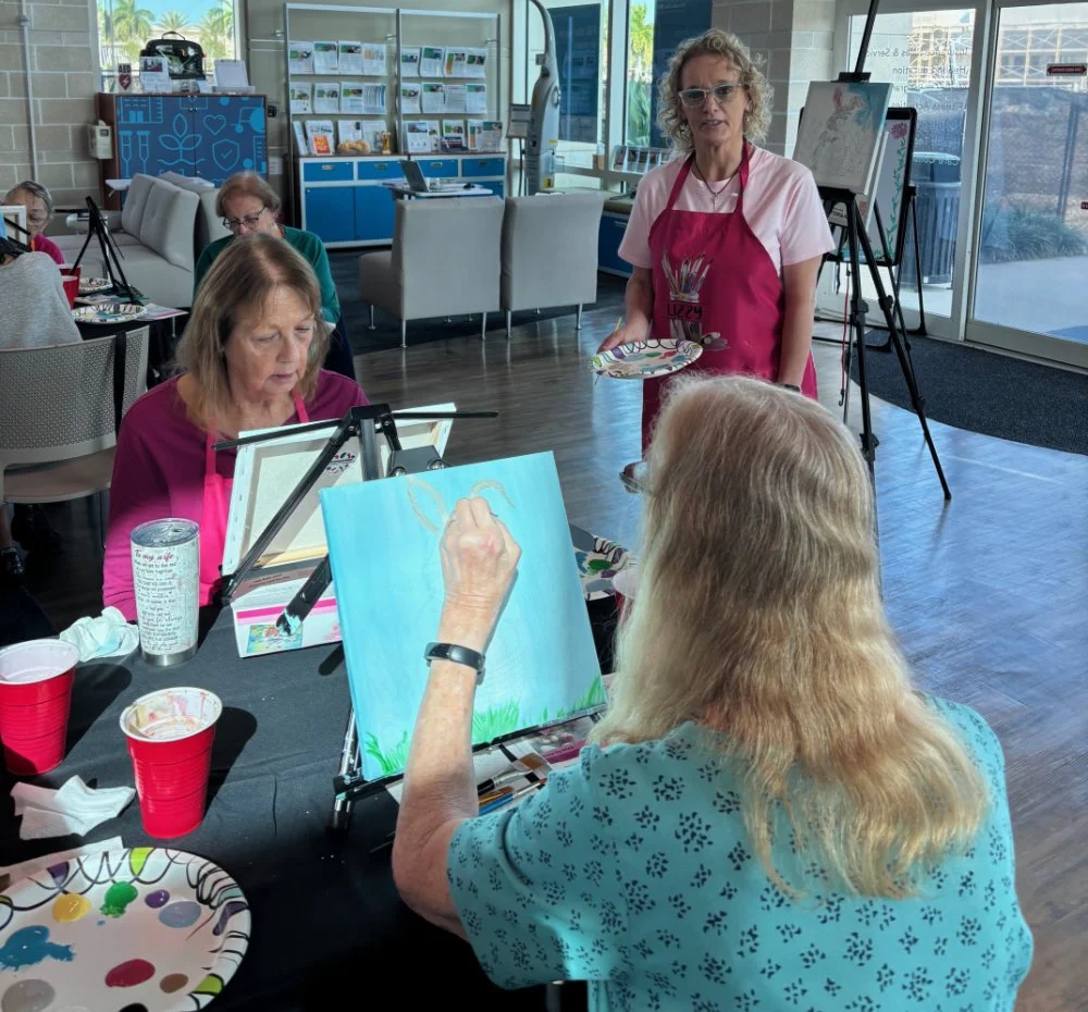 Women painting and socializing in a windowed art studio or community center.