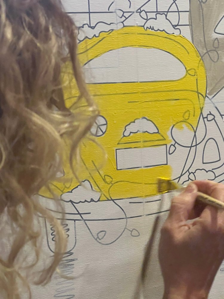 Person painting a yellow cartoon van on a large canvas with black outlines and clouds.