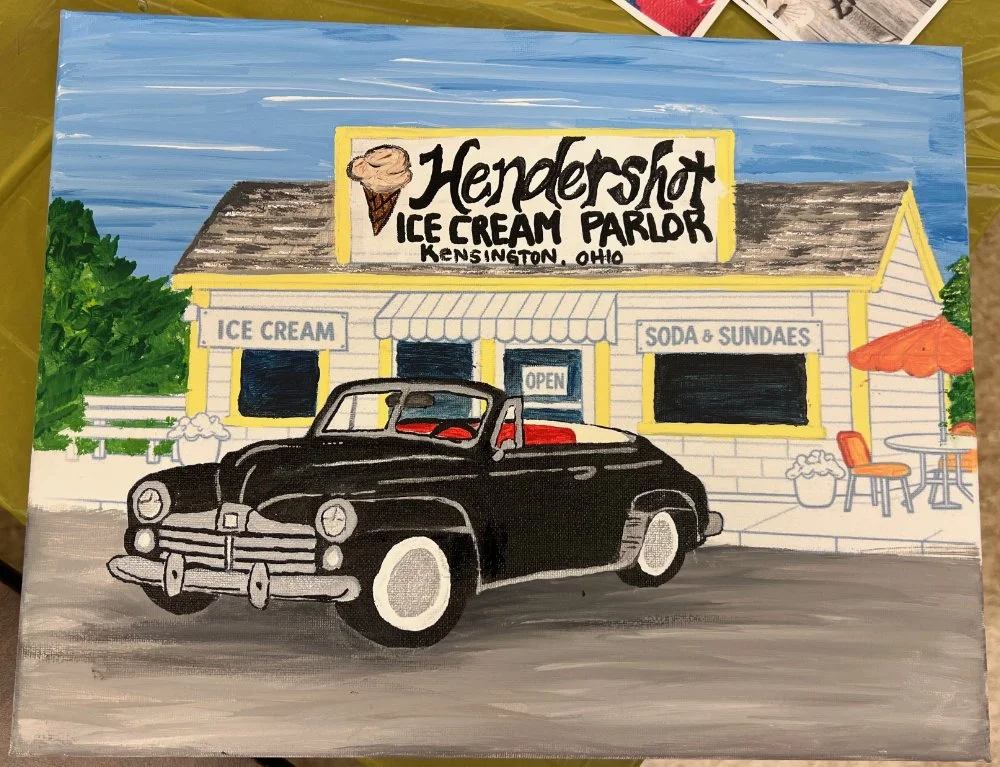 Painting of a black vintage car parked in front of Hendershot Ice Cream Parlor in Kensington, Ohio. The building features signs for ice cream, soda, and sundaes, with an outdoor seating area and umbrella.