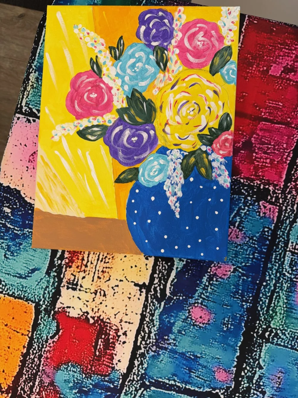 A colorful painting of a flower bouquet in a blue polka-dot vase against a vibrant yellow background.