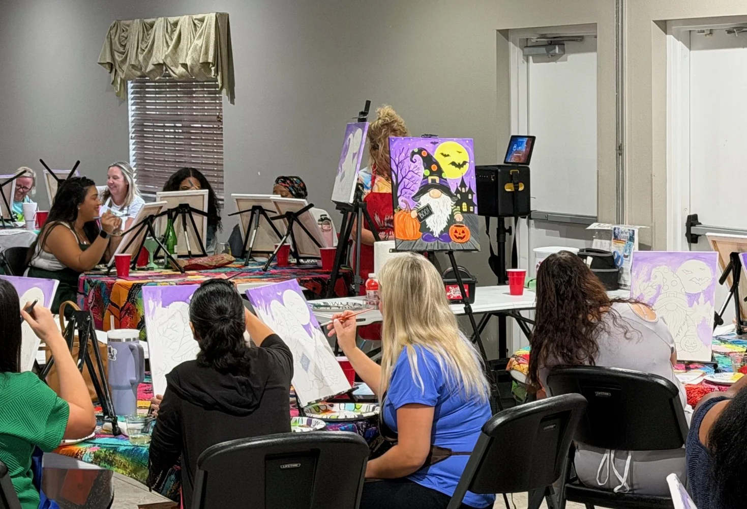 People participating in a pumpkin painting event, with Halloween-themed paintings on display and decorations on the table.