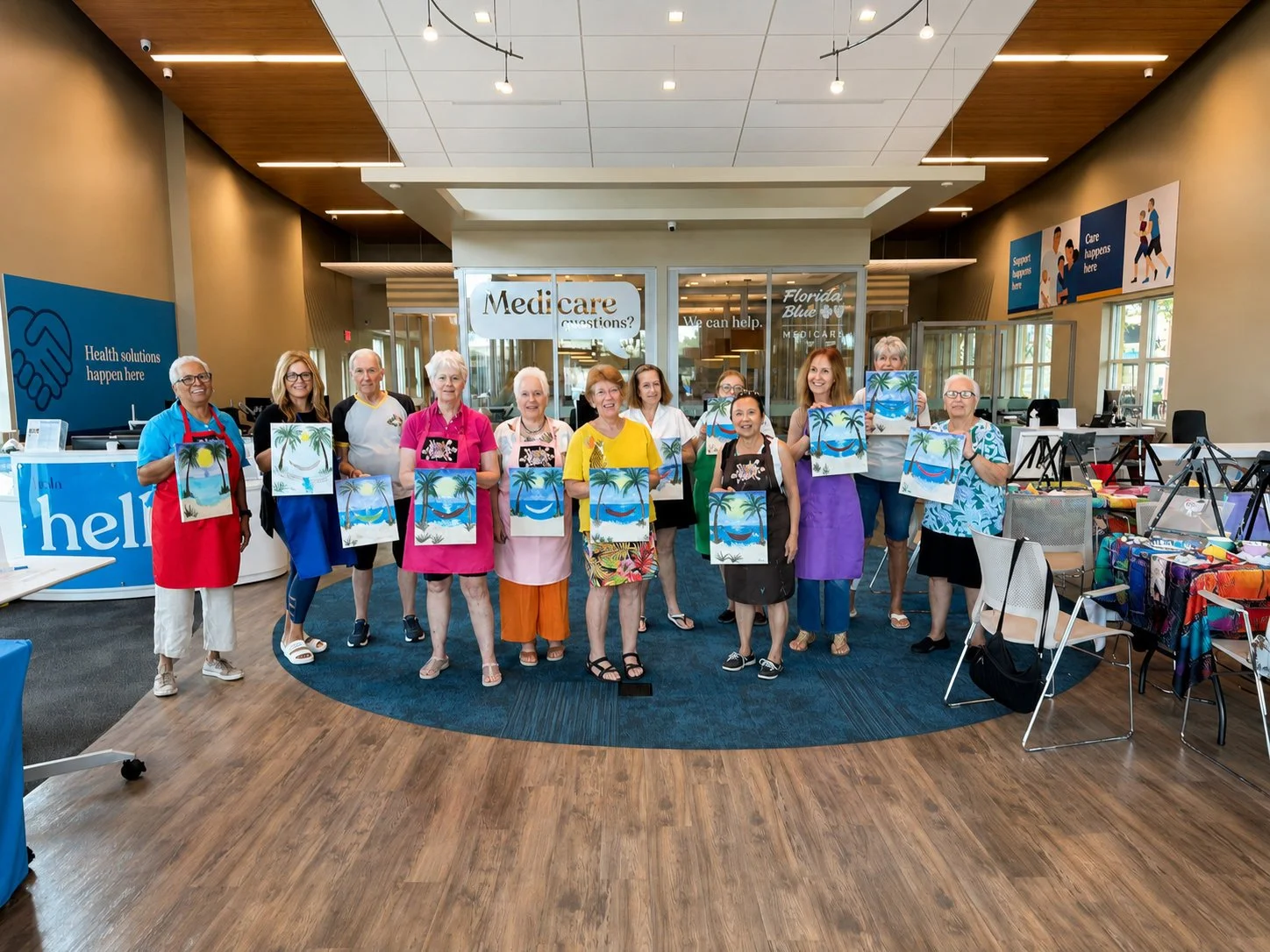 Group of people in an indoor space holding paintings of tropical beaches and palm trees.
