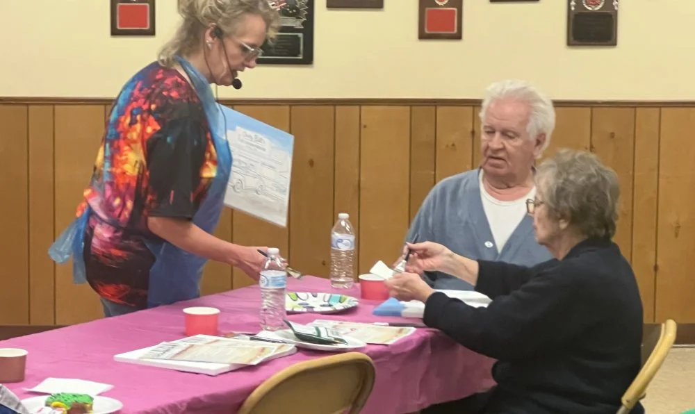 A woman serving food at a table to an elderly man and woman in a room with wooden paneling and framed pictures on the wall.