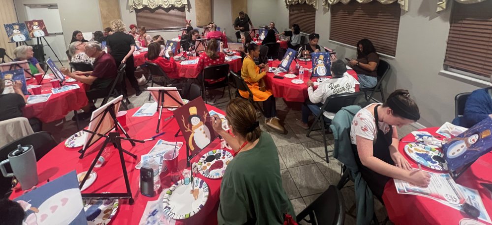 People participating in a snowman painting class at a holiday-themed event.
