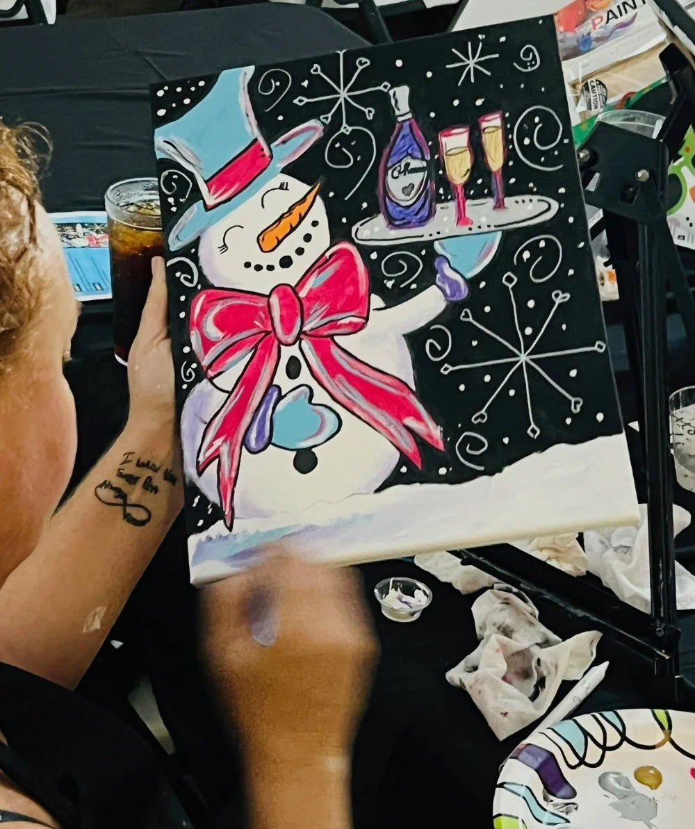A person holding a clock with a snowman painting behind it, wearing a red bow tie, and a pink top hat, surrounded by holiday and snowflake designs, with glasses of champagne on a tray.