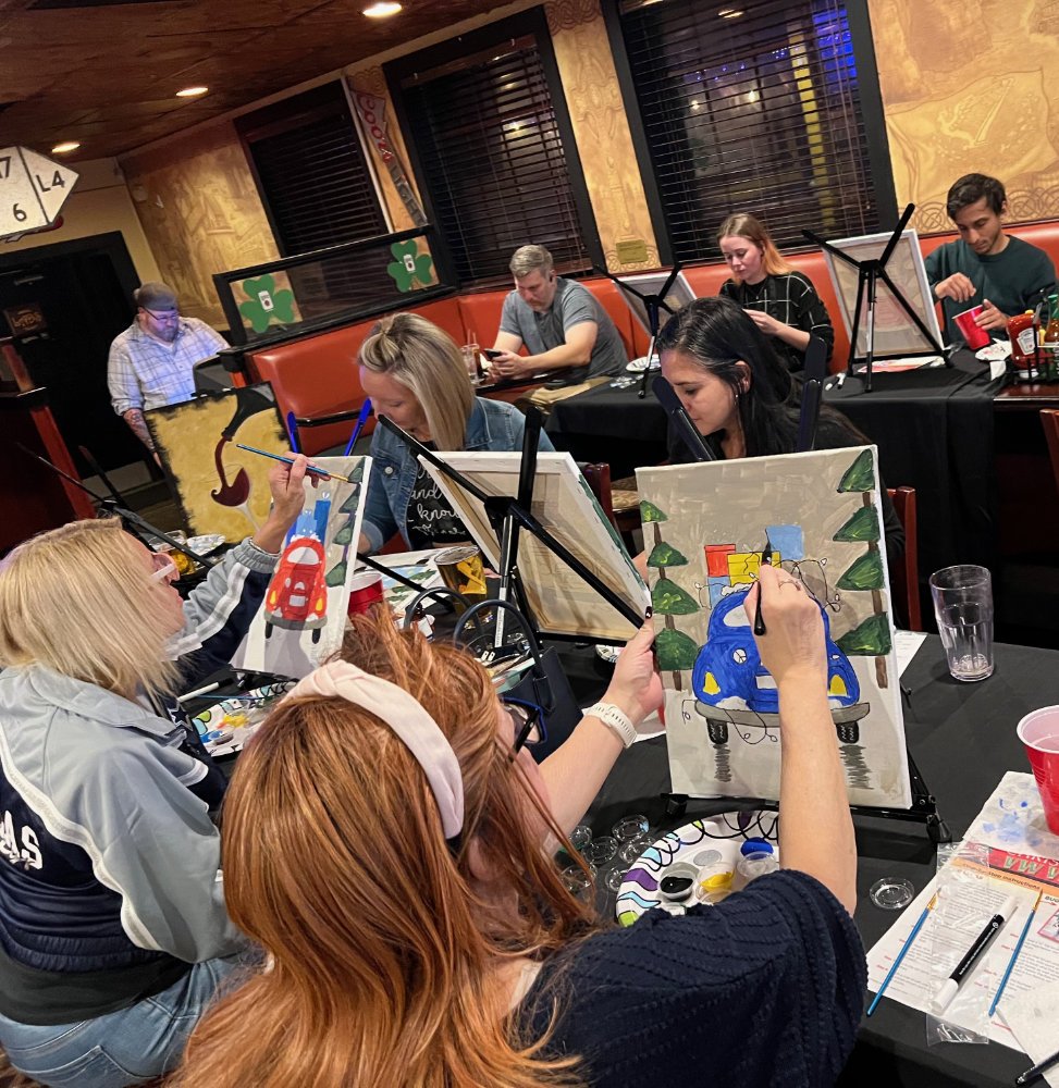 People participating in a paint and sip event, painting cars on canvases in a cozy indoor setting.