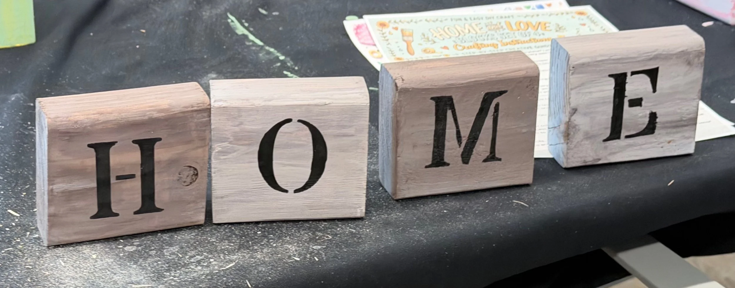 Wooden blocks spell out the word 'HOME' on a black surface.